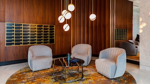 A modern lobby with wooden paneling, a seating area with two armchairs and a coffee table, and a wall-mounted light fixture. - Brabank Residence by HappyStay (Gdansk)