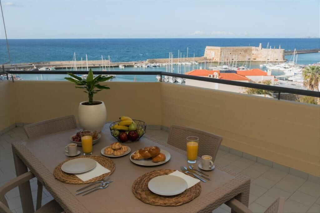 Un balcón con una mesa lista para el desayuno, con vista a un puerto deportivo y al mar.