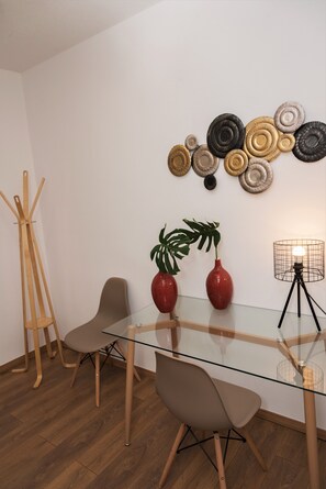 A modern dining area with a glass table, two chairs, a floor lamp, and decorative wall art. - Koules Sea View City Apartment (Heraklion)
