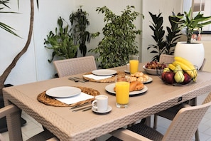 A breakfast table set with plates, a glass of orange juice, a bowl of fruit, and a basket of bananas. - Koules Sea View City Apartment (Heraklion)