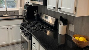 Una cocina moderna con armarios blancos, encimera negra, electrodomésticos de acero inoxidable y una ventana con persianas.