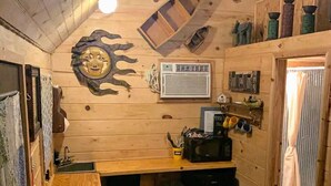 Een compact houten blokhutje met een klein kitchenette, een plafondventilator en een rustieke inrichting, waaronder een spiegel in de vorm van een zon.
