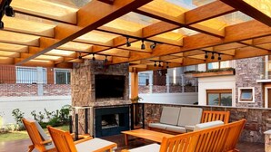 Una terrazza esterna con arredi in legno, un camino in pietra e una TV a parete.