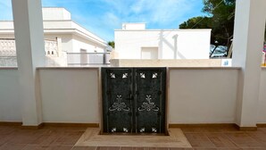 A covered outdoor area with a tiled floor, a white wall, and a black gate with white floral designs. - Appartamento Murena 8 (Squinzano)