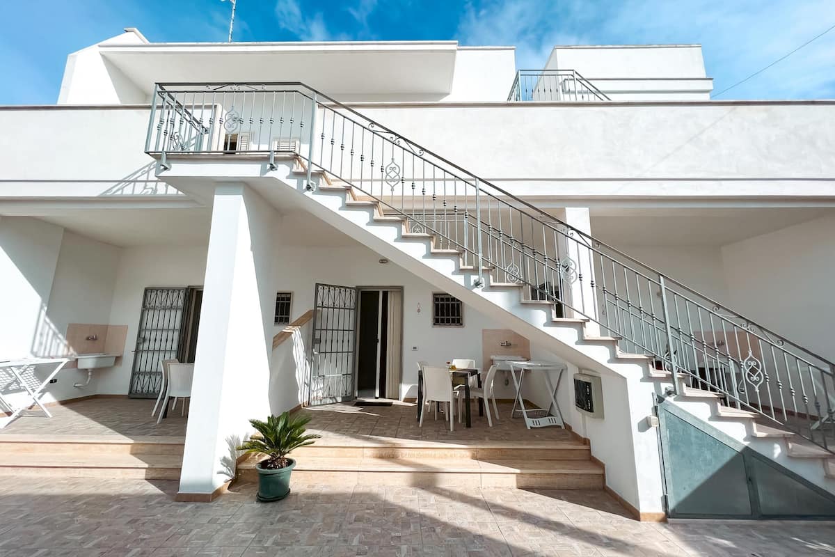 Ein modernes, zweistöckiges Haus mit Treppe, Balkon und kleiner Sitzgelegenheit im Freien.