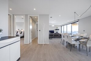 A modern kitchen with white cabinets and a wooden countertop. There is a dining area with a table set for four and a large window offering a view of the ocean. - Tower Penthouse by Homie (Funchal)