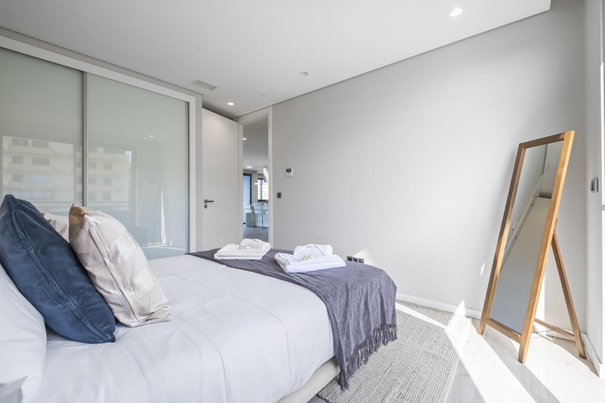 A modern bedroom with a bed, pillows, a mirror, and a sliding door leading to a bathroom.