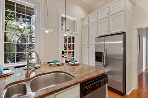 A kitchen with white cabinets, a stainless steel refrigerator, a double sink, and pendant lighting.