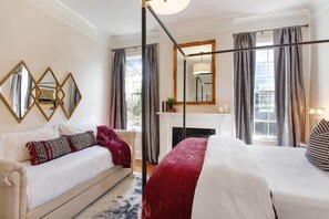 A hotel room with a bed, a sofa, a fireplace, and large windows with curtains.