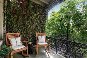 A balcony with two wooden rocking chairs, a black metal railing, and a wall covered with green foliage.