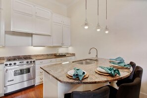 A kitchen with white cabinets, a stainless steel stove, granite countertops, a sink, and a dining area with chairs.