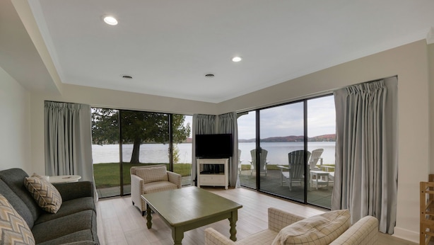 A spacious living room with a large TV, comfortable seating, and a view of a lake.