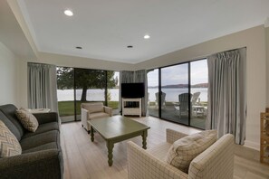 Un salón amplio con un televisor grande, asientos cómodos y vistas a un lago.