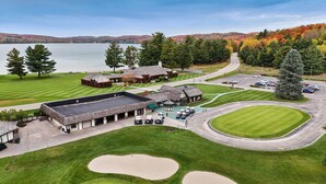 A golf course with a clubhouse, a parking area, and a lake in the background.