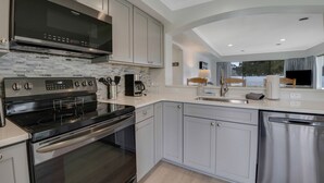 A modern kitchen with stainless steel appliances, white cabinetry, and a large window offering a view of the outdoors.