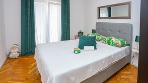 Een net opgemaakt bed met een witte dekbedovertrek, een groen kussen en een klein vat ernaast.