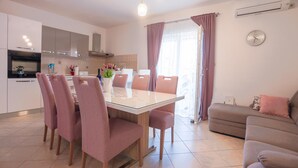 Een moderne keuken met witte kasten, een eettafel met roze stoelen en een bruine bank.