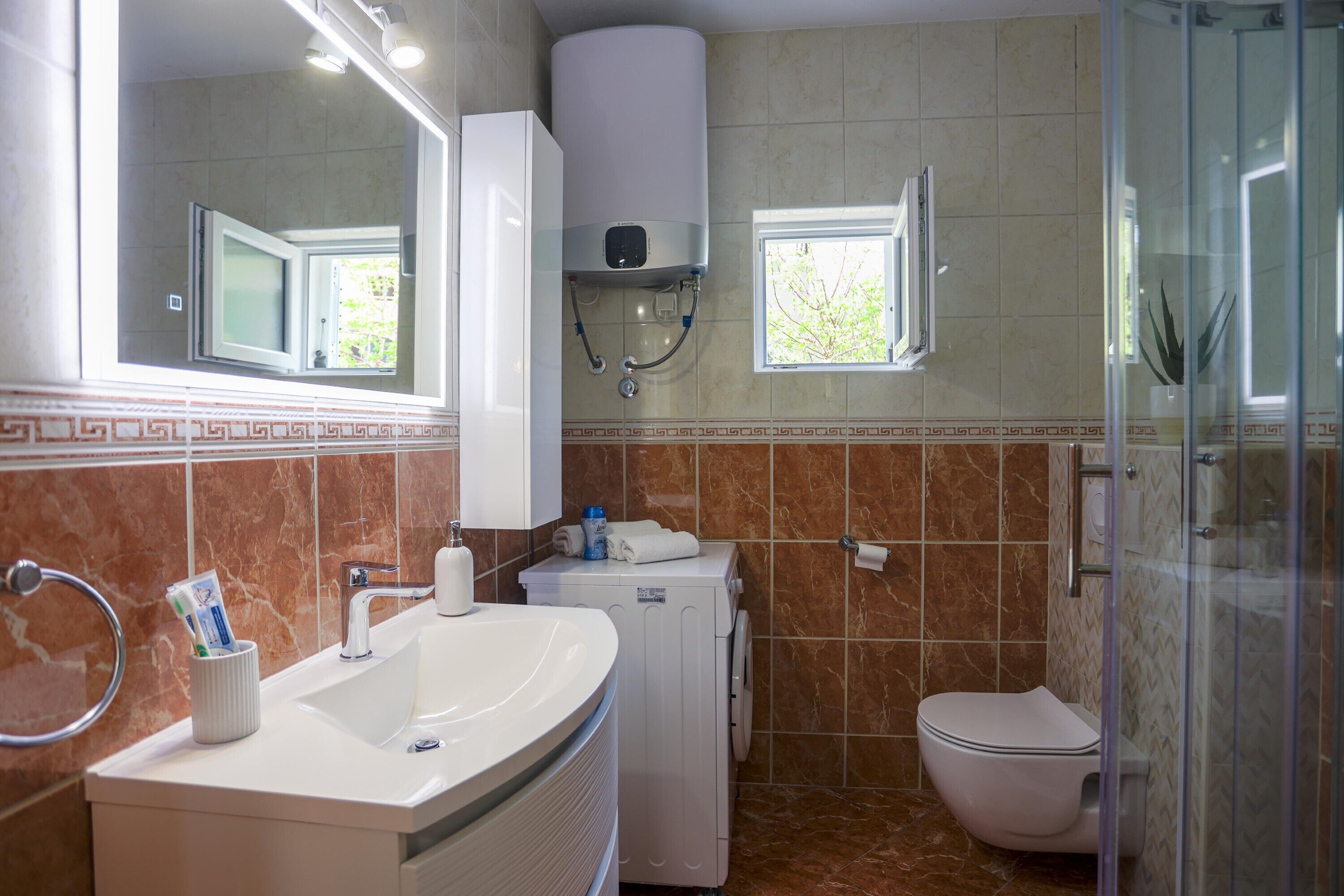 A bathroom with a sink, mirror, toilet, and shower area.