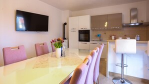 Een moderne keuken met witte kasten, een flatscreen televisie en een eethoek met een marmeren tafel en roze stoelen.