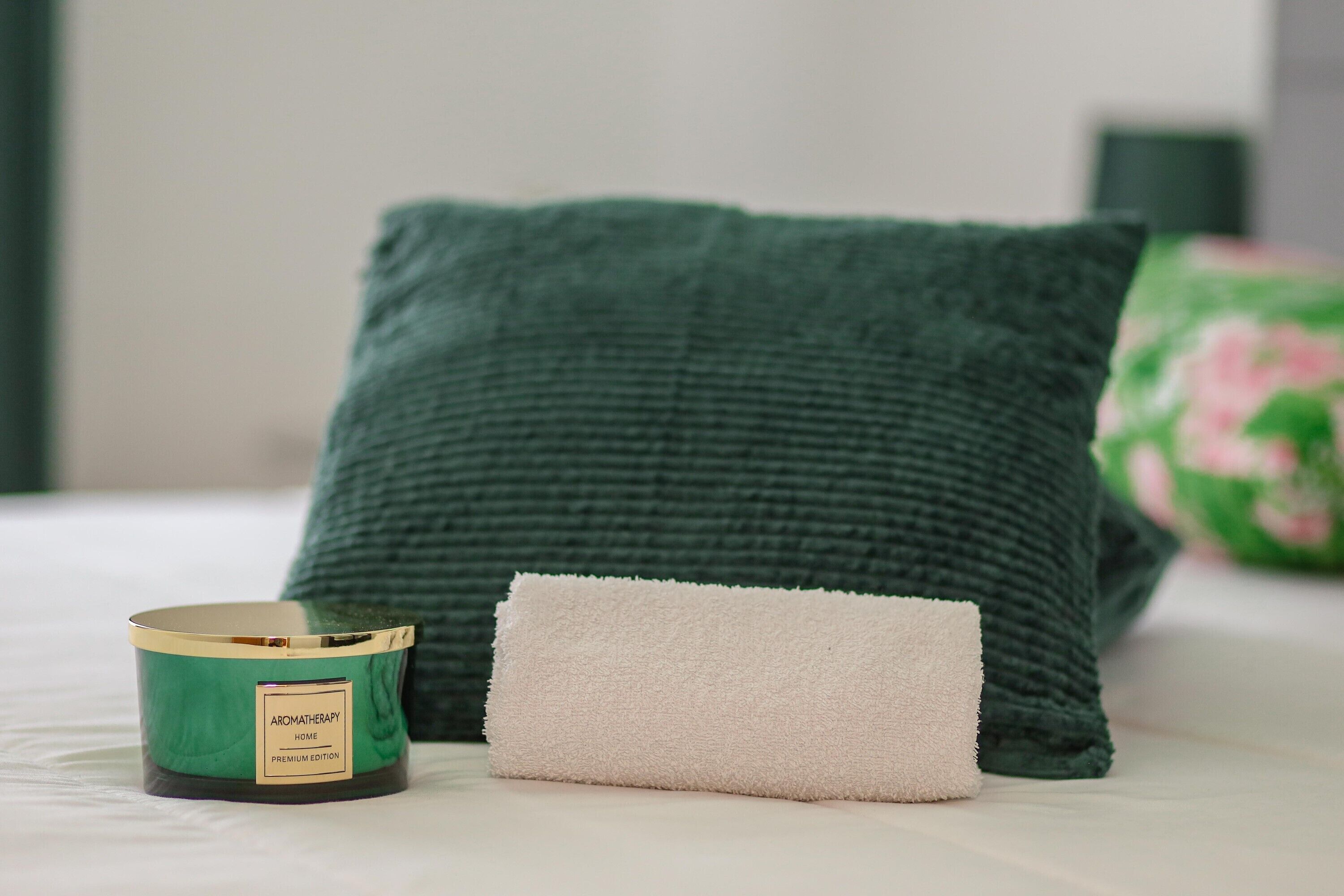 A green textured pillow, a white towel, and a green scented candle on a bed.