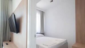 Un dormitori amb un llit, un televisor penjat a la paret i una finestra amb cortines.