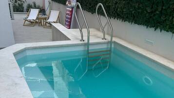 En swimmingpool med krystalklart blåt vand, en metalstige og liggestole.
