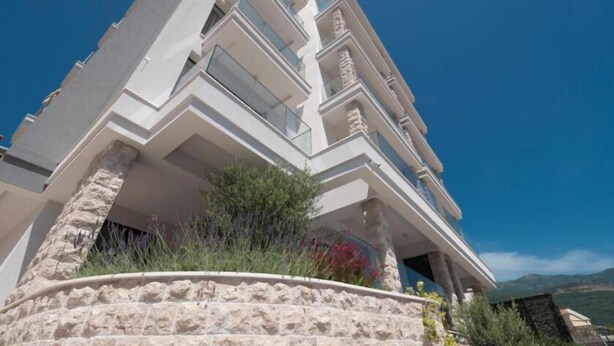 Un edifici de diversos pisos amb balcons, una base de pedra i un cel blau clar al fons.