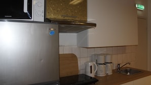 A compact kitchen with a stainless steel refrigerator, a microwave, a coffee maker, and a sink.