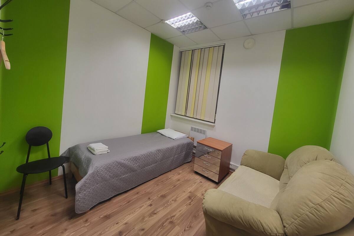 A room with a bed, a chair, a dresser, and a window with blinds.