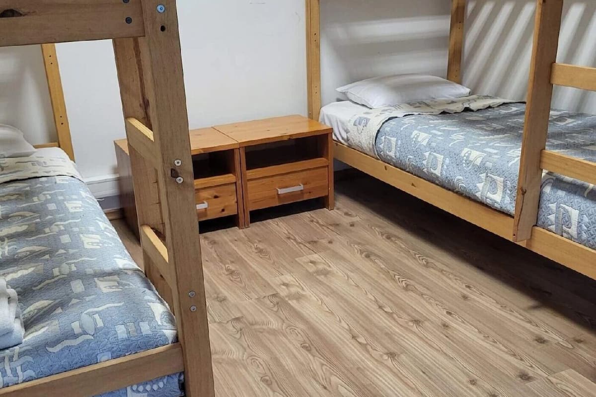 A room with two bunk beds, a wooden nightstand with drawers, and a patterned bedspread.