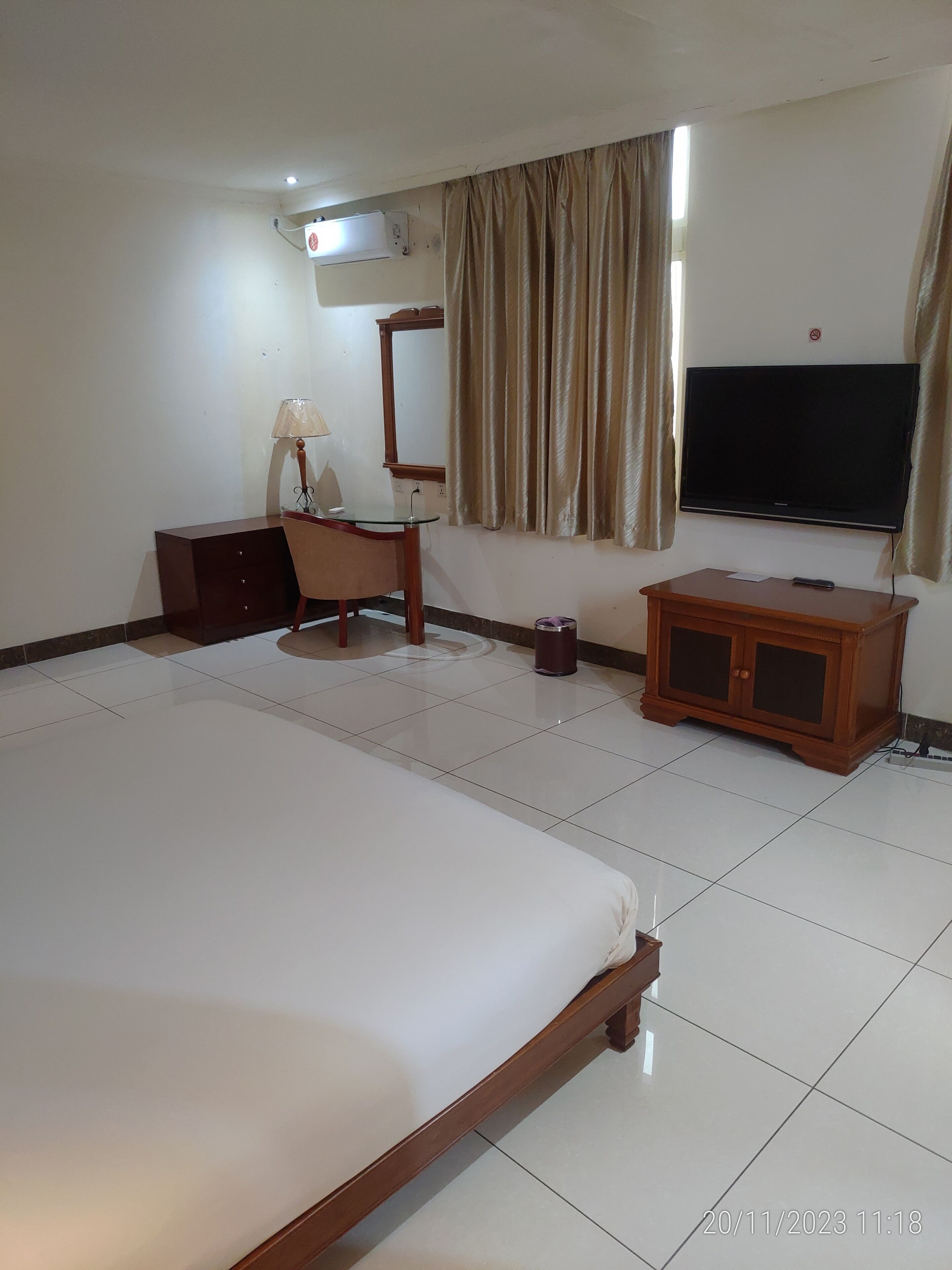 A hotel room with a large bed, a desk with a chair, a television, and a cabinet.