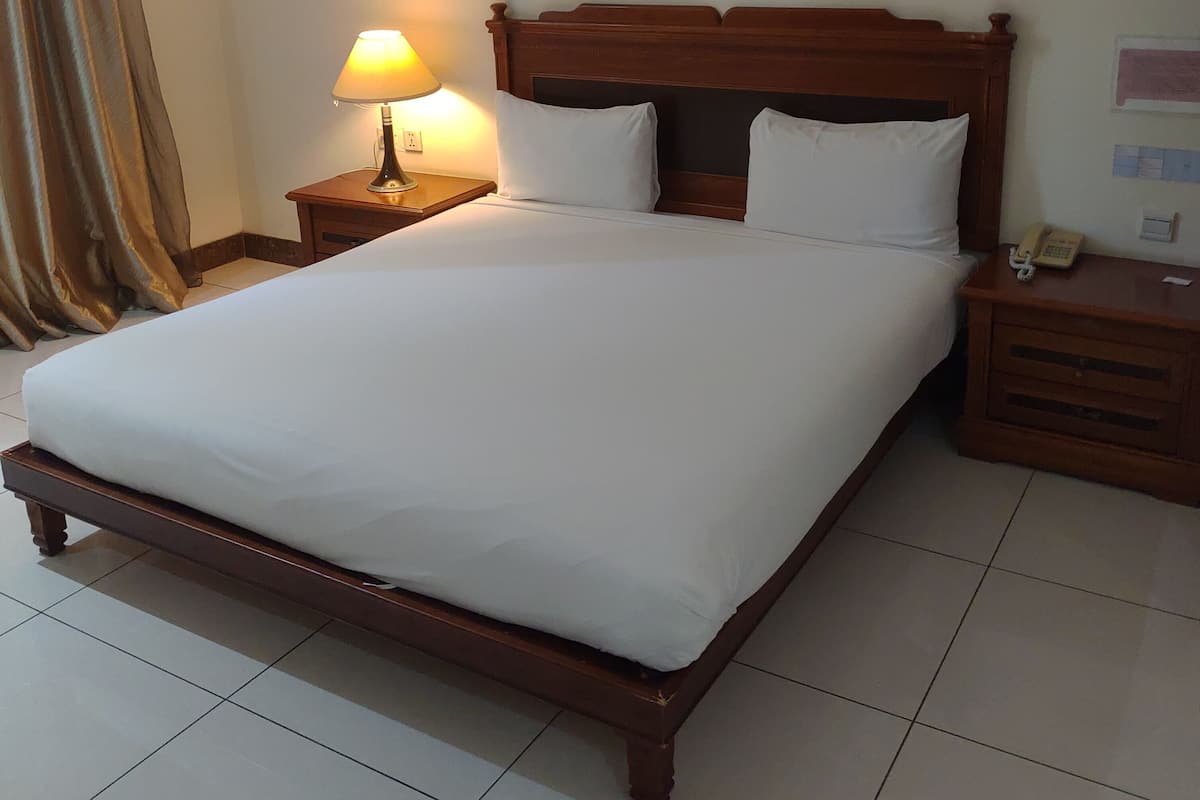 Una cama bien hecha con sábanas blancas, un cabecero de madera y una lámpara de noche.
