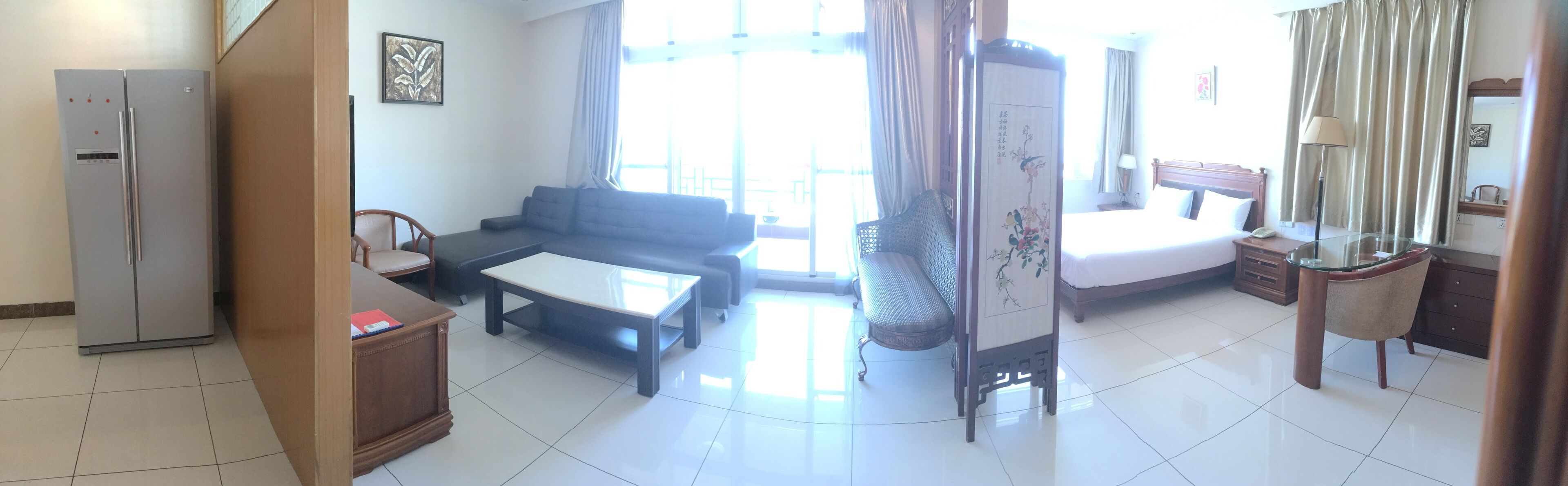 Una habitación de hotel con cama, sofá, mesa de comedor, refrigerador y una ventana grande.