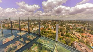 A high vantage point view of a cityscape with buildings and greenery, viewed through a glass floor. - Lux Suites Le marc Luxury Apartments (Nairobi)