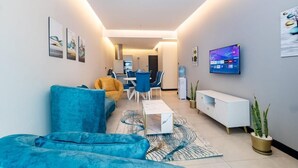 A modern living room with a blue sofa, a coffee table, and a TV on the wall. - Lux Suites Le marc Luxury Apartments (Nairobi)