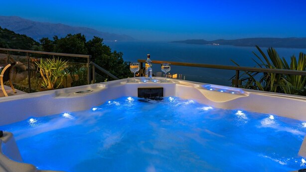 Een hottub met uitzicht op zee en bergen, omringd door groen.