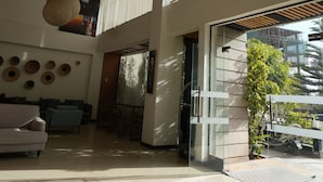 Un vestíbulo espacioso con techo alto, modernas lámparas colgantes, una zona de estar con sofás y vistas al exterior a través de amplias ventanas.