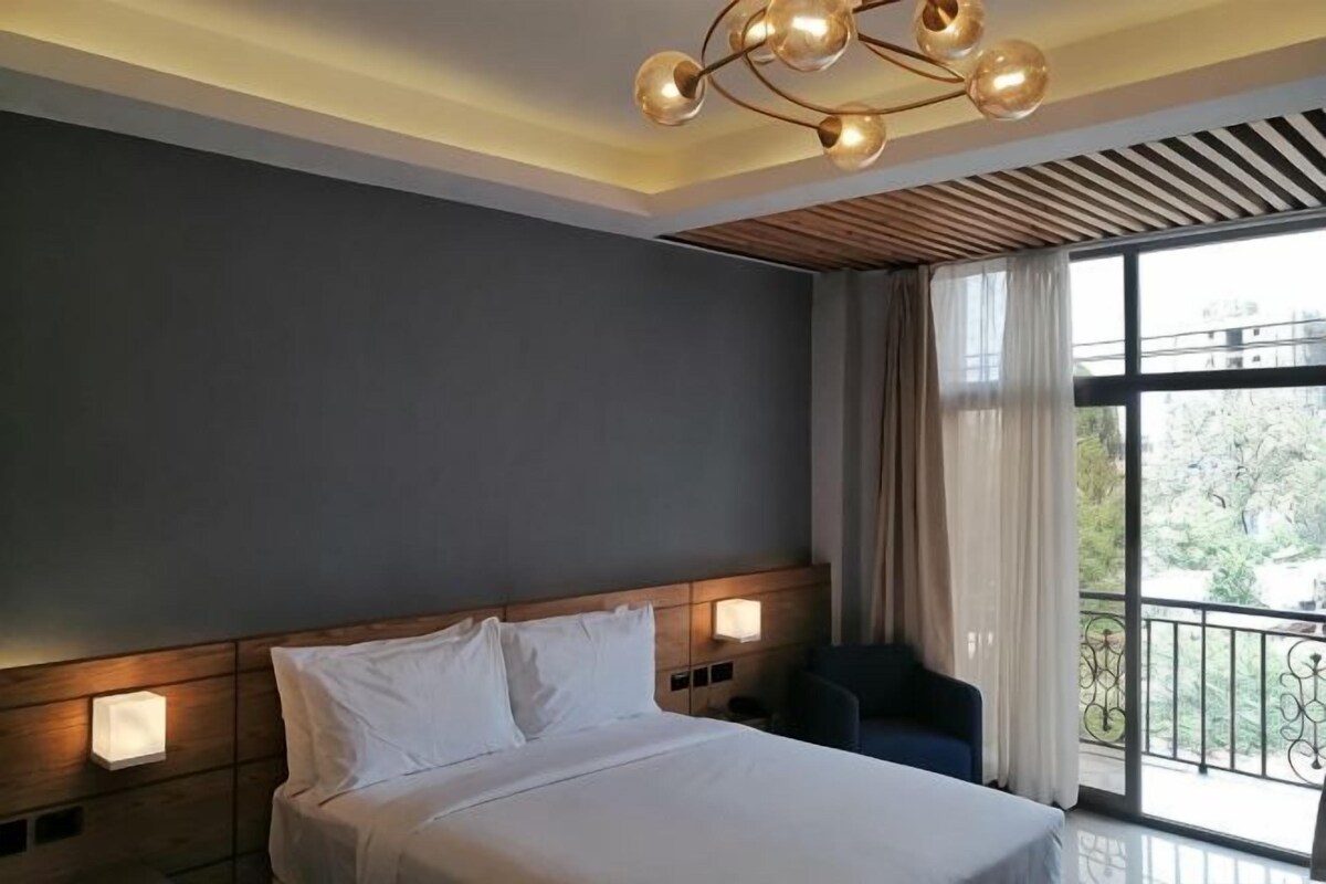 A modern hotel room with a large bed, a view of the outdoors, and a unique ceiling light fixture.