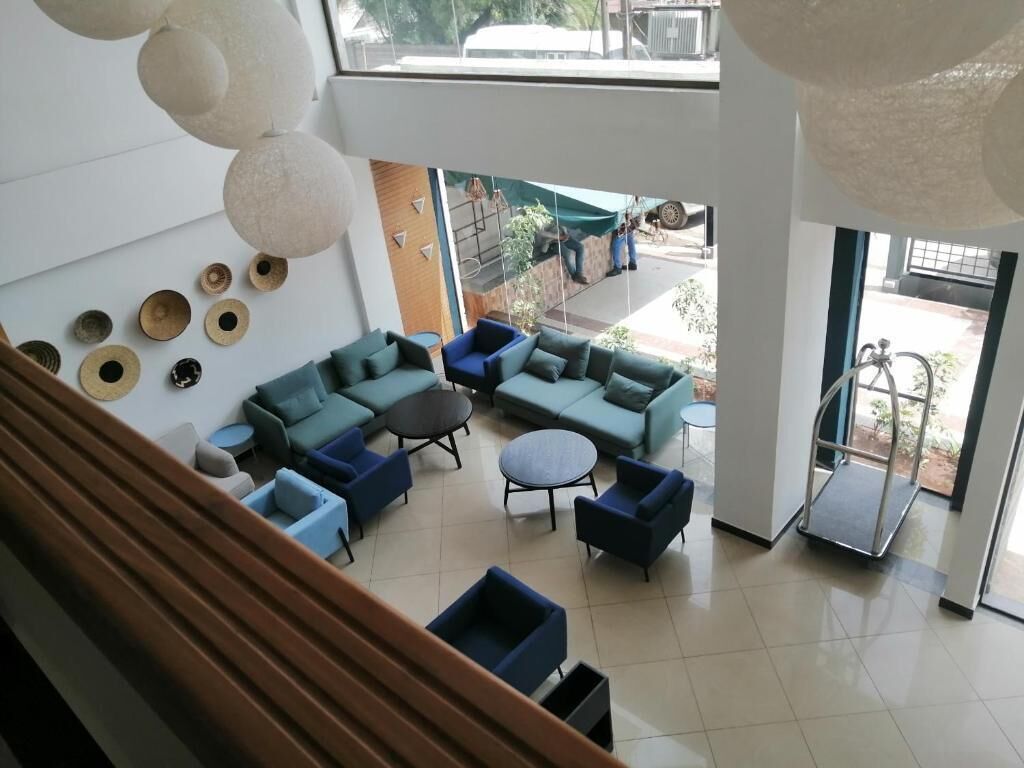 A spacious indoor area with a large sofa set, multiple chairs, and a coffee table. There are decorative wall elements and a view of the outside through large windows.