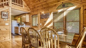 A wooden cabin interior with a dining area, kitchen, and a staircase leading to an upper level. - Enchanted View Lodge 3 Bedroom Cabin by RedAwning (Gatlinburg)