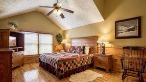 A bedroom with a wooden bed, two bedside tables with lamps, a ceiling fan, a large window with blinds, a wooden dresser, and a framed picture on the wall. - Enchanted View Lodge 3 Bedroom Cabin by RedAwning (Gatlinburg)