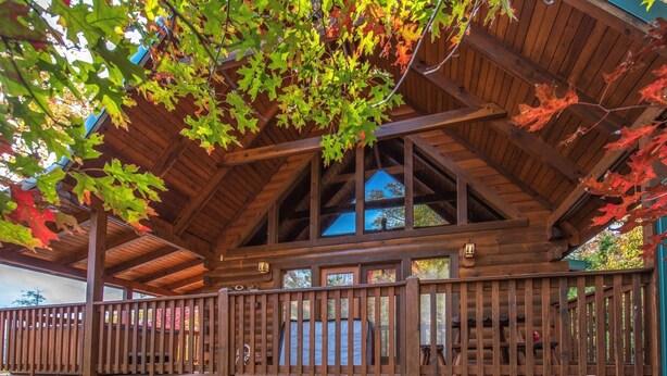 A wooden deck with a stone foundation, a covered area with a wooden ceiling, and a view of the surrounding trees. - Enchanted View Lodge 3 Bedroom Cabin by RedAwning (Gatlinburg)