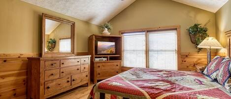 A bedroom with a wooden dresser, a bed with a quilt, a ceiling fan, and a television on a wooden cabinet.