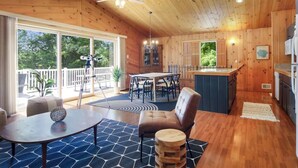 A wooden cabin interior with a dining area, kitchen, and large windows. - Tavi Haus: Lakefront~Kayaks~SUP~Sauna~Pool Table (Empire)