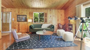 A cozy cabin interior with a wooden ceiling, a green sofa, a round coffee table, and a telescope on a tripod. - Tavi Haus: Lakefront~Kayaks~SUP~Sauna~Pool Table (Empire)