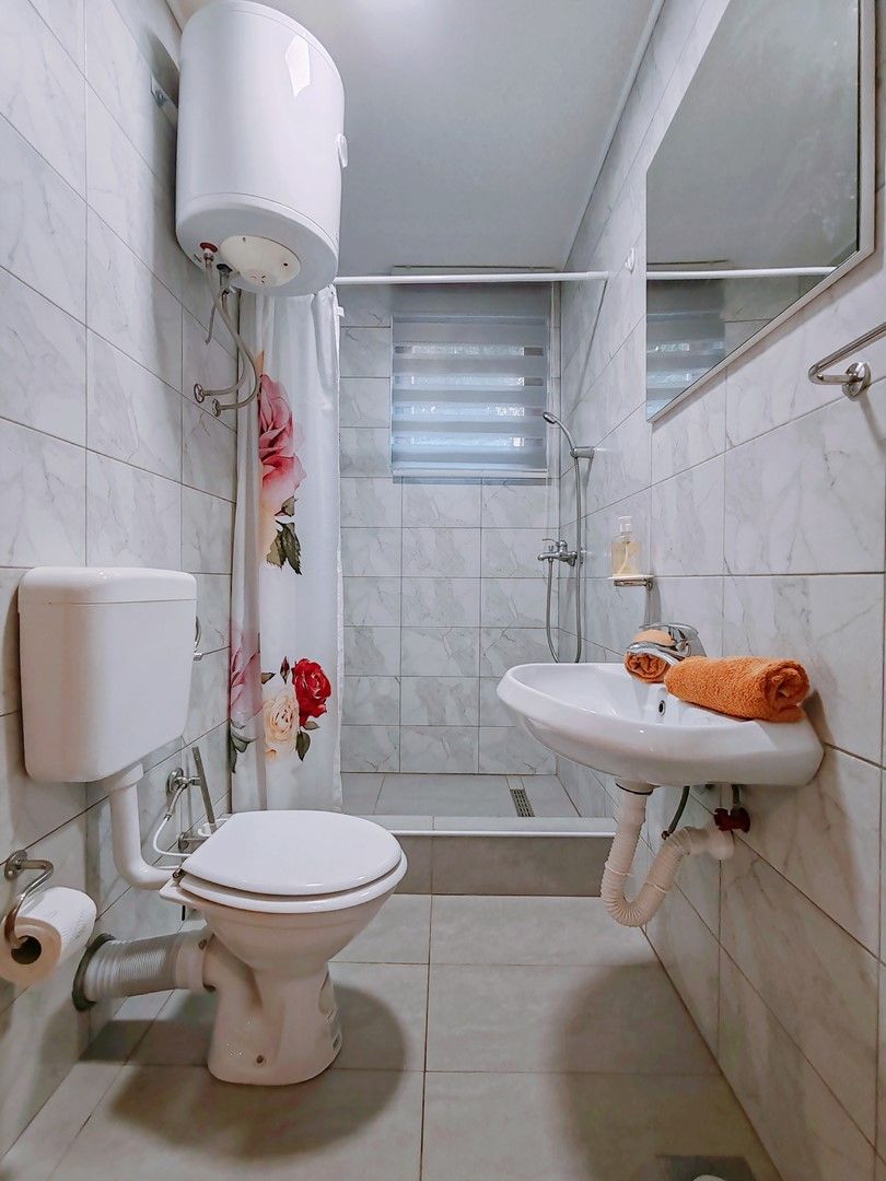 A bathroom with a toilet, sink, shower, and a toilet paper holder.