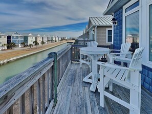 Une terrasse en bois avec une table et des chaises, donnant sur un canal et une rangée de maisons.