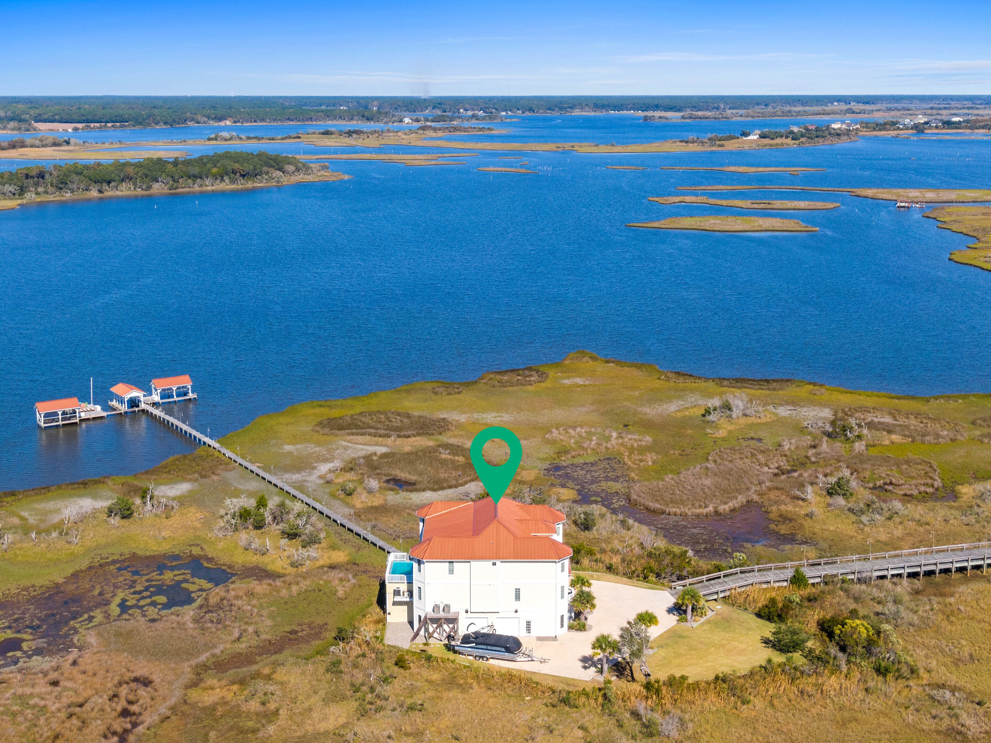 An aerial view of a coastal area with a white building with a red roof, a dock with boats, and a green location marker.