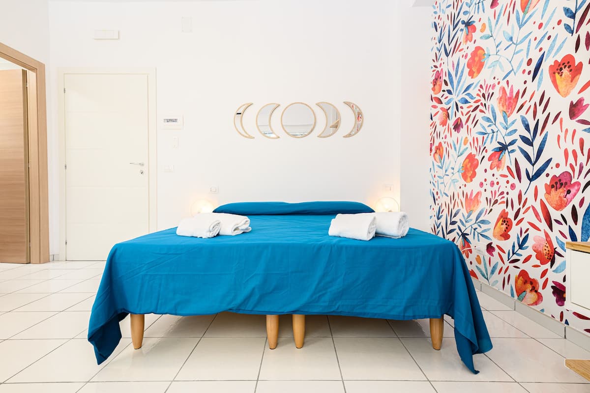 Une pièce avec un lit, deux serviettes, une porte et un mur orné d’un motif floral.