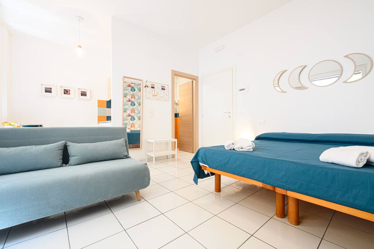 Une chambre d’hôtel moderne avec un canapé, un lit recouvert d’une courtepointe bleue et une petite table.